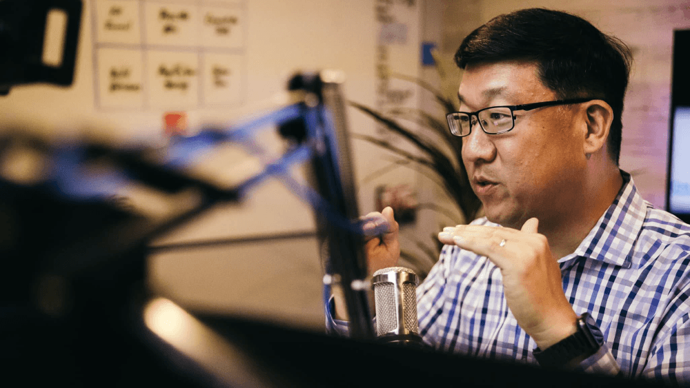 Portrait of a man speaking into a microphone in a recording studio setting.