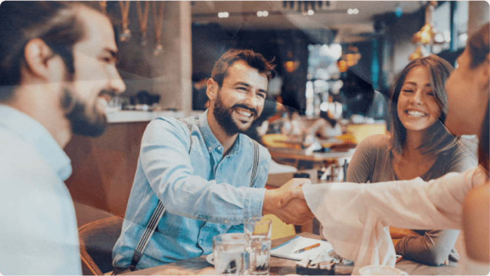 Group of smiling young adults talking and laughing over coffee at a bright, modern café.