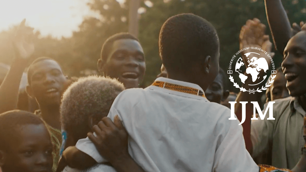 A group of people celebrate together next to the IJM logo.