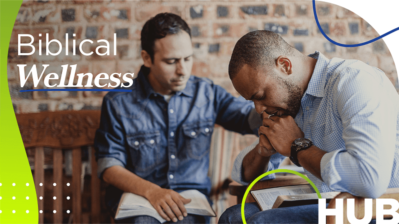 Two men sit close together in prayer, one supporting the other, over a Bible on a table with the text "Biblical Wellness Hub" overlaid.