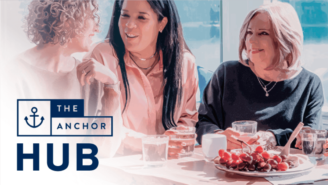 Three women sit at a well-lit café table smiling and talking, with the logo "The Anchor Hub" overlaid in the corner.