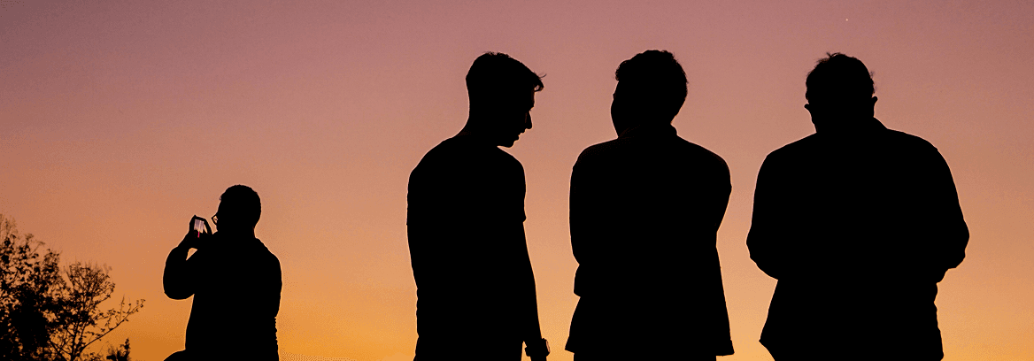 Silhouettes of four men talking and photographing at sunset.
