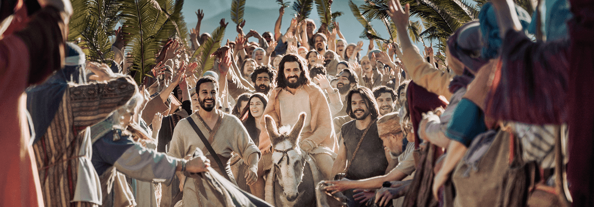 Jesus rides a donkey through a cheering crowd waving palm branches.