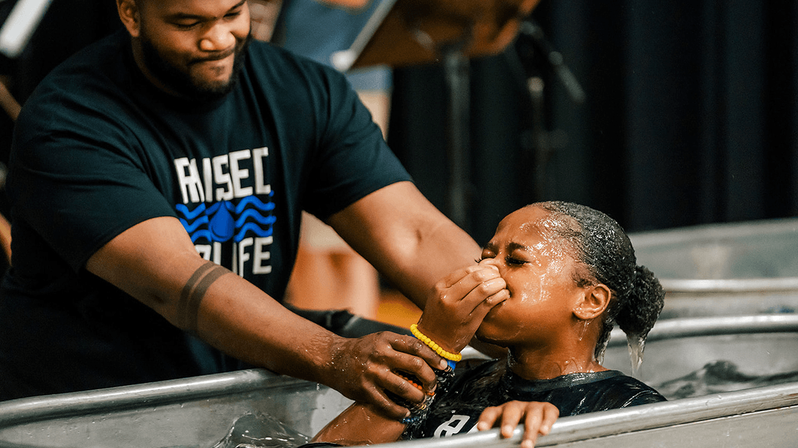 Man performing baptism for a woman in a baptismal pool at a church event.