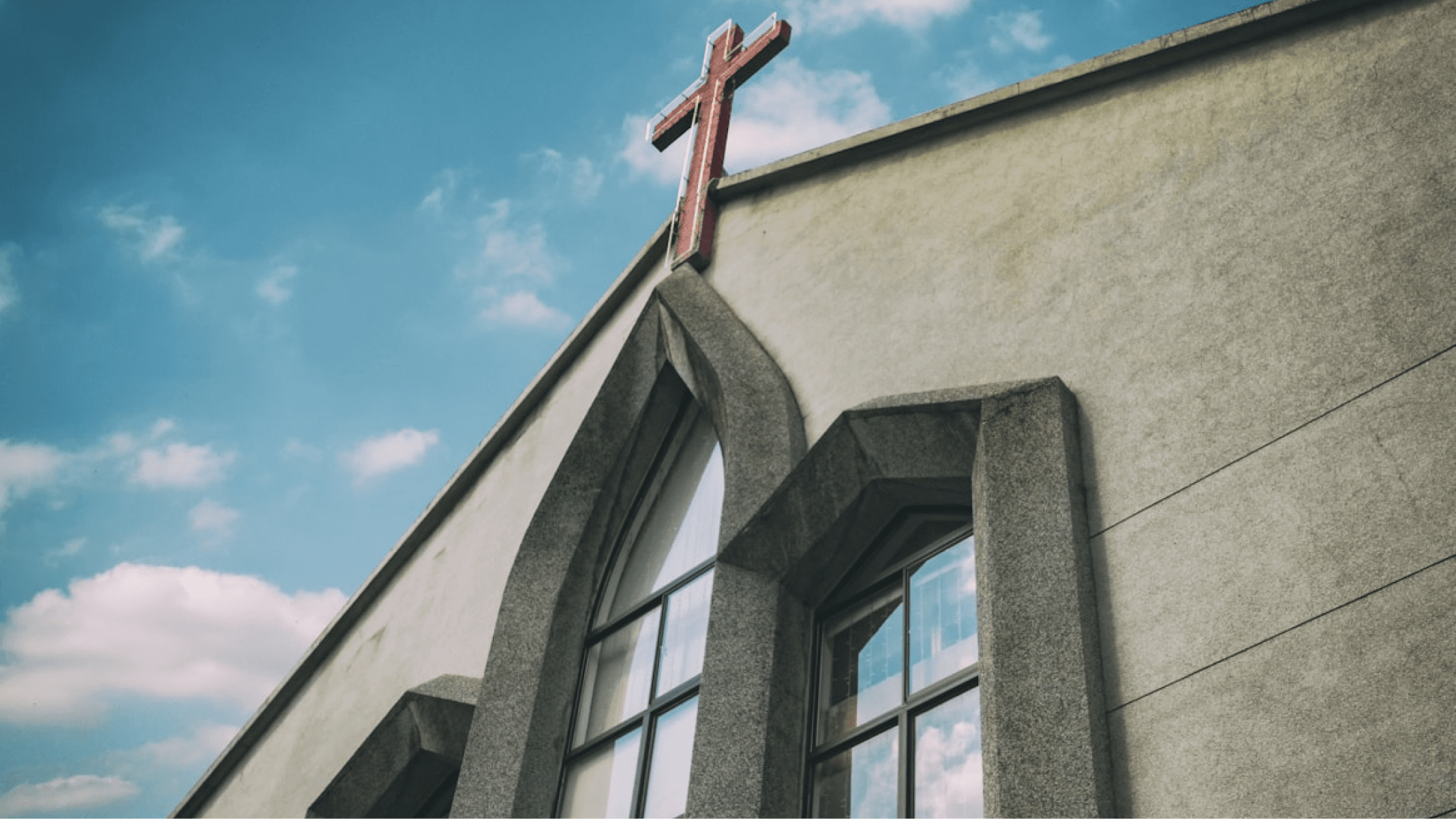 Exterior of a church building with a red cross on the roof.